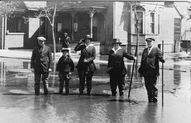 <B>High water in Beardstown</B> in this undated photograph (possibly 1922). People are carrying poles to guide them through any deep spots in the water as they cross flooded roads.