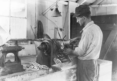 <b>Blank Cutting</b>, 1931.<br>The man cutting the blanks is using tongs to hold the shell in place with one hand and operating the pusher with the other.
