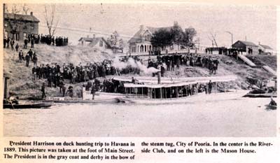 <b>The President Comes Duck Hunting</b> in Havana, 1889.  Caption reads "President Harrison on duck hunting trip to Havana in 1889.  This picture was taken at the foot of Main Street.  The President is in the gray coat and derby in the bow of the steam tug, City of Peoria.  In the center is the Riverside Club, and on the left is the Mason House."  Also in enlargements.<br>Mason County Democrat Bicentennial Issue, 1976.