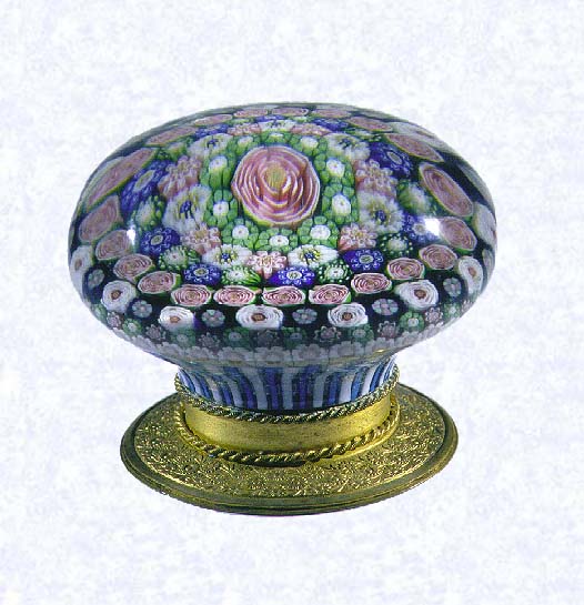 <B>Close Concentric Millefiori on Gilded Base (side view)<BR>France<BR>Clichy, base dated 1845</B><BR>Diameter: 7.3 cm (2 7/8 inches)<BR>(702323)<BR><BR>Close concentric millefiori with six rings of millefiori canes in deep purple, green, pink, and white around a pink Clichy rose; fourth row contains twenty-one pink Clichy roses; fifth ring contains thirteen white Clichy roses; pedestal column of blue and white staves; gilded metal foot (which could have been added at any time) engraved 