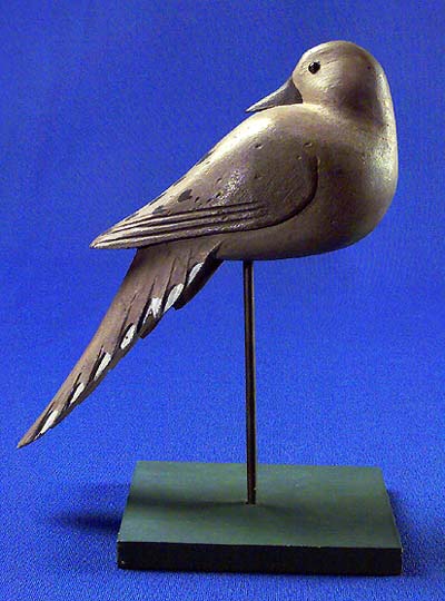 <b>Dove Decoy</b>, circa 1940-50.<br>Frank Cassini, Galesburg, Illinois.  <br>Balsa wood, 8 1/2 inches high by 9 3/4 inches long.  <br>Illinois State Museum Collection (1958.77, 798908)<br>Gift of Joseph French, St. Louis, Missouri.<p> Frank Cassini (1899-1967) was a prolific carver of prey and confidence decoys for forty years.  He produced more that 5,000 decoys.  He made several examples of dove decoys of balsa wood. The decoys were hung in trees from a string attached to a screwhook in their backs.  They are considered graceful works of folk art today.</p>