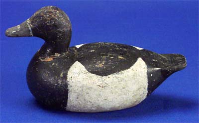 <b>Bluebill Drake Decoy</b>, no date.<br>Louis H. Hahn, Havana, Illinois.  <br>Wood, 11 3/4 inches long.<br>Illinois State Museum Collection (1967.42, 798984)<br>Gift of Herman Glick, Havana, Illinois.<p>Hahn was a market hunter who made solid wood decoys of ducks and geese between 1900 and 1920.  They are often crudely formed from telephone pole wood and painted without much detail. </p><p>He is known for using a human hunter decoy when hunting geese in marshes.  He positioned this cutout man at the opposite end of the marsh, pulled a wire to raise it to a standing position, thus flushing the geese toward him.