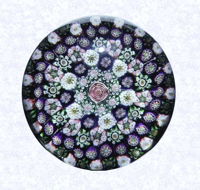 <B>Close Concentric Millefiori with Nineteen Clichy Roses<BR>France<BR>Clichy, circa 1845-55</B><BR>Diameter: 8 cm (3 1/8 inches)<BR>(702278)<BR><BR>Close concentric millefiori with six concentric rings of millefiori canes in deep purple, pink, green, and white around a pink Clichy center rose; eighteen white Clichy roses alternate with green canes in the second outermost ring; pink and white stave basket