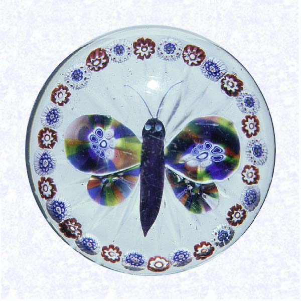 <B>Lampworked Butterfly<BR>France<BR>Baccarat, circa 1845-55</B><BR>Diameter: 8 cm (3 1/8 inches)<BR>(702339)<BR><BR>Lampworked butterfly with a deep purple body, black head, light blue eyes, and multicolored sliced millefiori cane wings; encircled by a ring of alternating red and white millefiori canes; star-cut base
