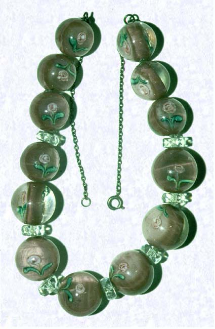 <B>Lampworked Bead Necklace<BR>Czechoslovakia (attributed)<BR>factory unknown, early twentieth century</B><BR>Length: 41.5 cm (16 1/2 inches)Largest Bead: 1.9 cm (3/4 inch)<BR>(702490)<BR><BR>Glass bead necklace comprised of thirteen beads; each containing two lampworked pink roses with green leaves; set on a mauve ground; beads alternate on a nylon cord with seven faceted clear bead discs; sterling silver chain