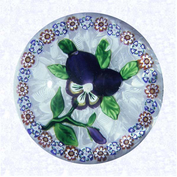 <B>Lampworked Pansy<BR>France<BR>Baccarat, circa 1845-55</B><BR>Diameter: 8 cm (3 1/8 inches)<BR>(702286)<BR><BR>Purple pansy blossom with a purple bud; eight green leaves and stem; encircled by a ring of alternating red and white, and blue, green, red, and white millefiori canes; on a white filigree ground